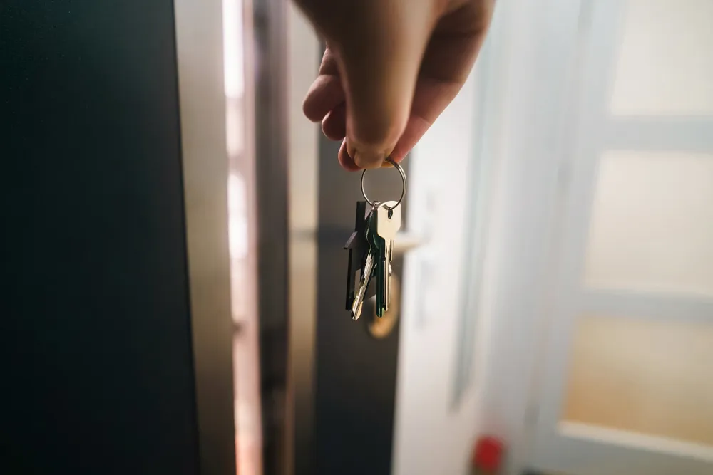 Hand holding house keys at an open front door